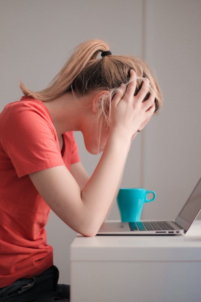 Young woman feeling stressed while studying at home with a laptop and coffee cup.